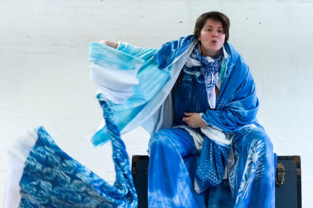 Claire, covered in blue blankets, twirls a blanket around in front of her until it looks like a whirlwind